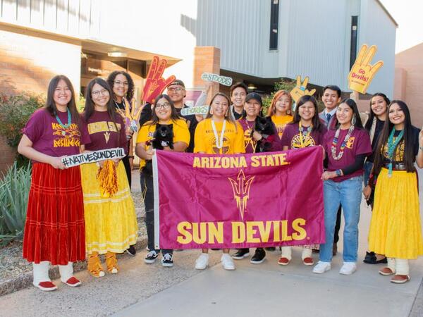 Native student sun devils dressed in ASU colors, holding and ASU banner, ASU foam hands, and #NativeSunDevil signs