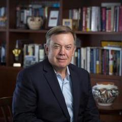 Michael Crow seated in office with bookshelf background
